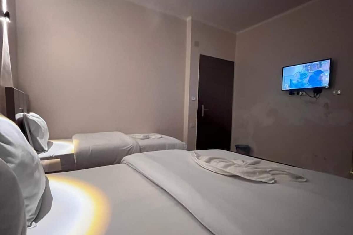 Quarto de hotel com uma cama, televisão fixada na parede e uma mesa de cabeceira.