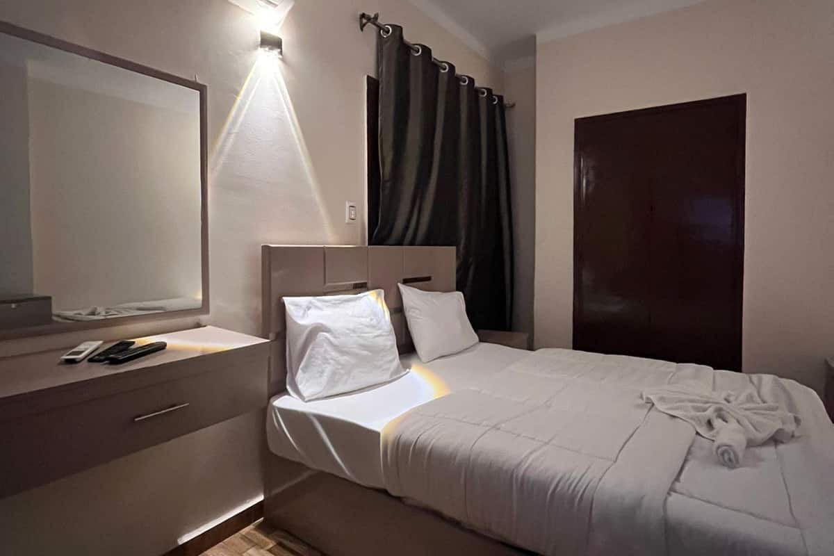Quarto de hotel com cama, mesa de cabeceira, espelho e aparelho de ar condicionado.