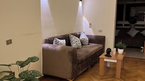 A modern living room with a herringbone wooden floor, a brown sofa with patterned cushions, and a small table with a plant and a sculpture. - Cairo casa inn (Cairo)