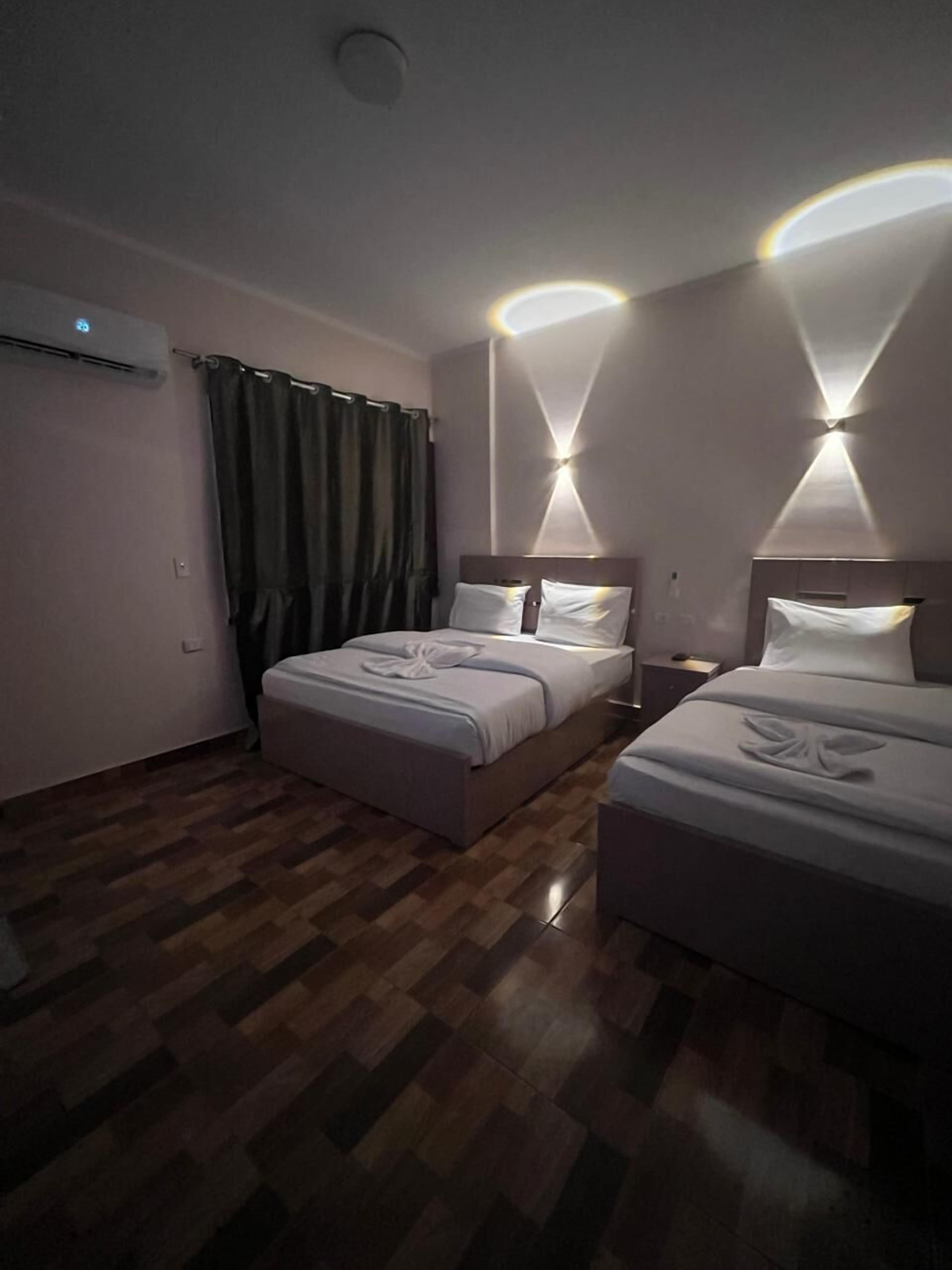 Habitación de hotel con dos camas, suelo de madera y lámpara de techo moderna.