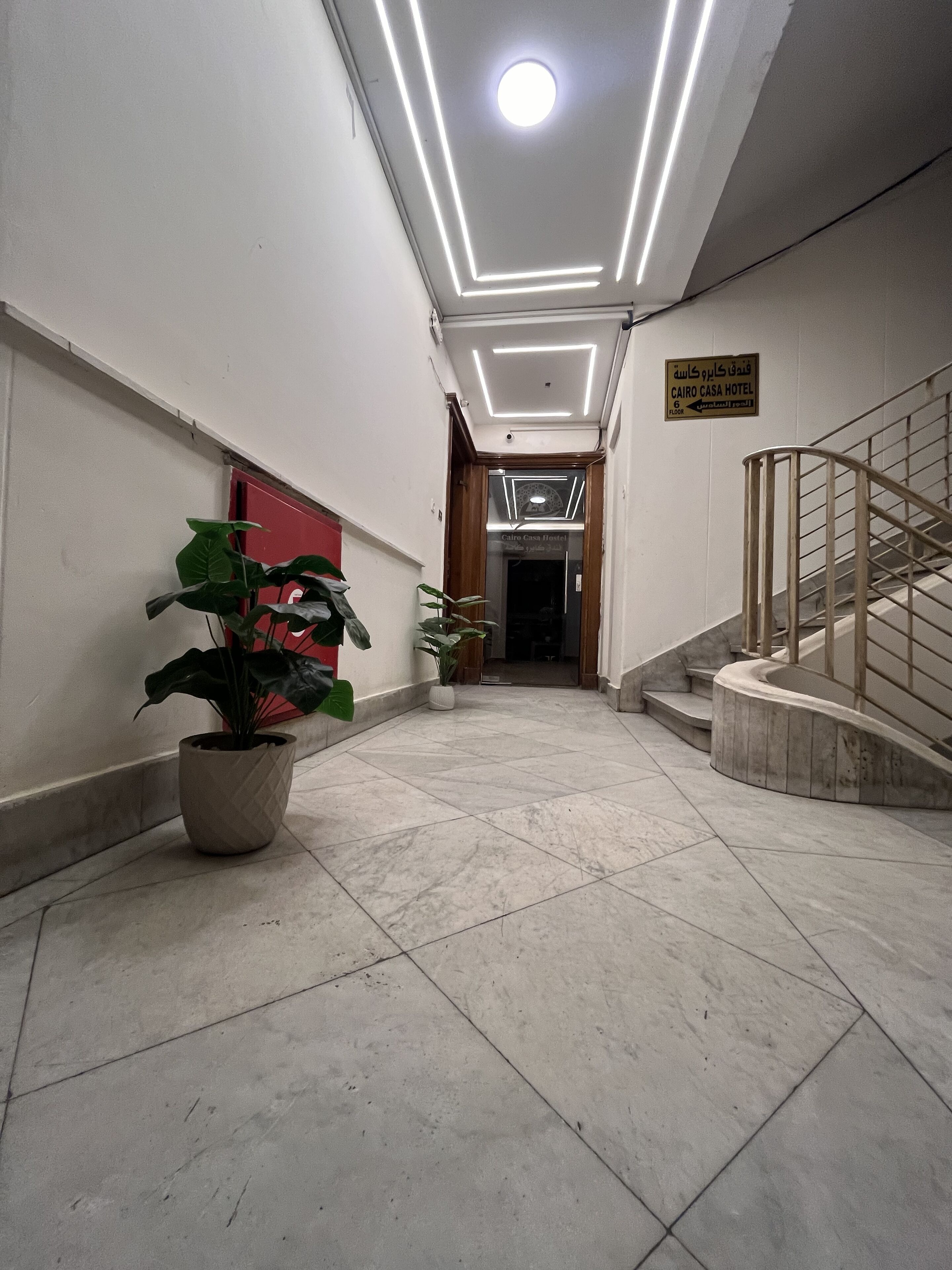 A hotel corridor with a potted plant, a staircase, and a sign indicating the location.