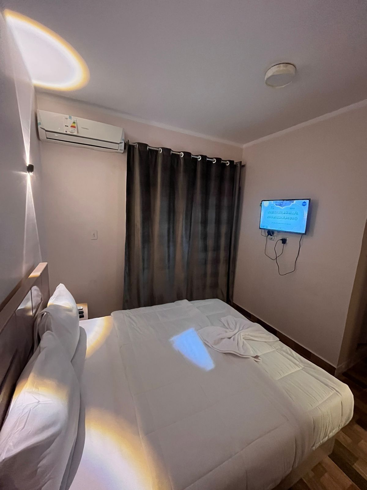 Quarto de hotel com uma cama, televisão fixada na parede e ar condicionado acima da cama.
