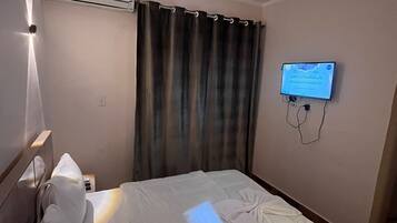 Quarto de hotel com uma cama, televisão fixada na parede e ar condicionado acima da cama.