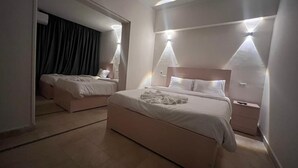 A hotel room with a large bed, a smaller bed, and a nightstand. There are two wall-mounted lights and a mirror above the bed. - Cairo casa inn (Cairo)