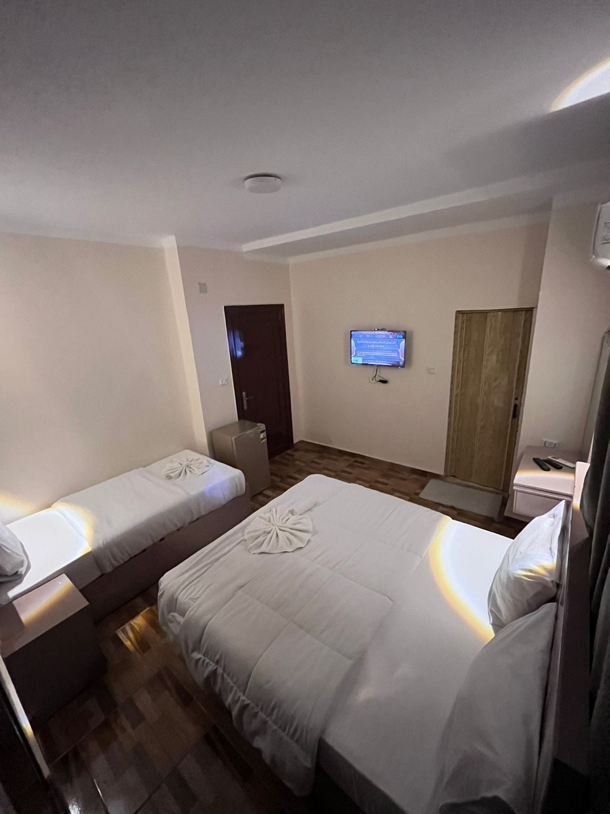 Habitación de hotel con dos camas individuales, un televisor en la pared y un escritorio pequeño con una silla.