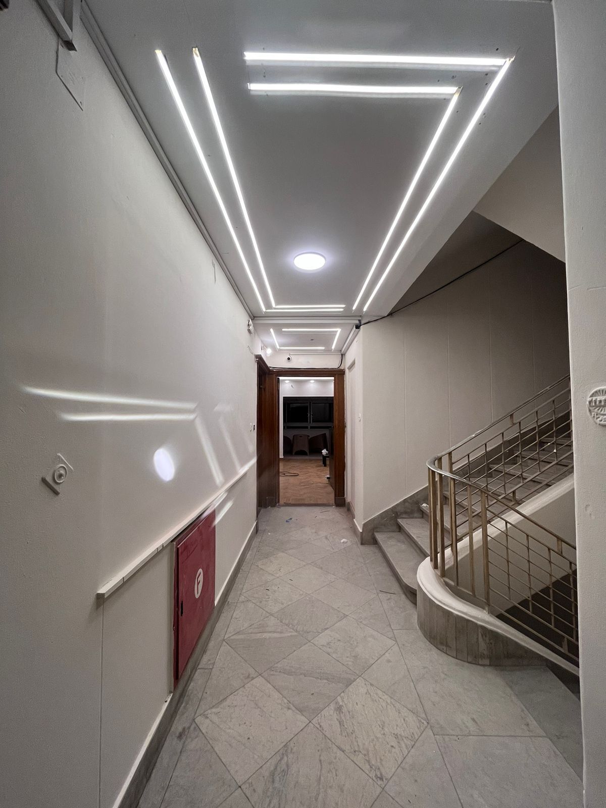 A corridor with a tiled floor, a red door, and a staircase with metal railings.