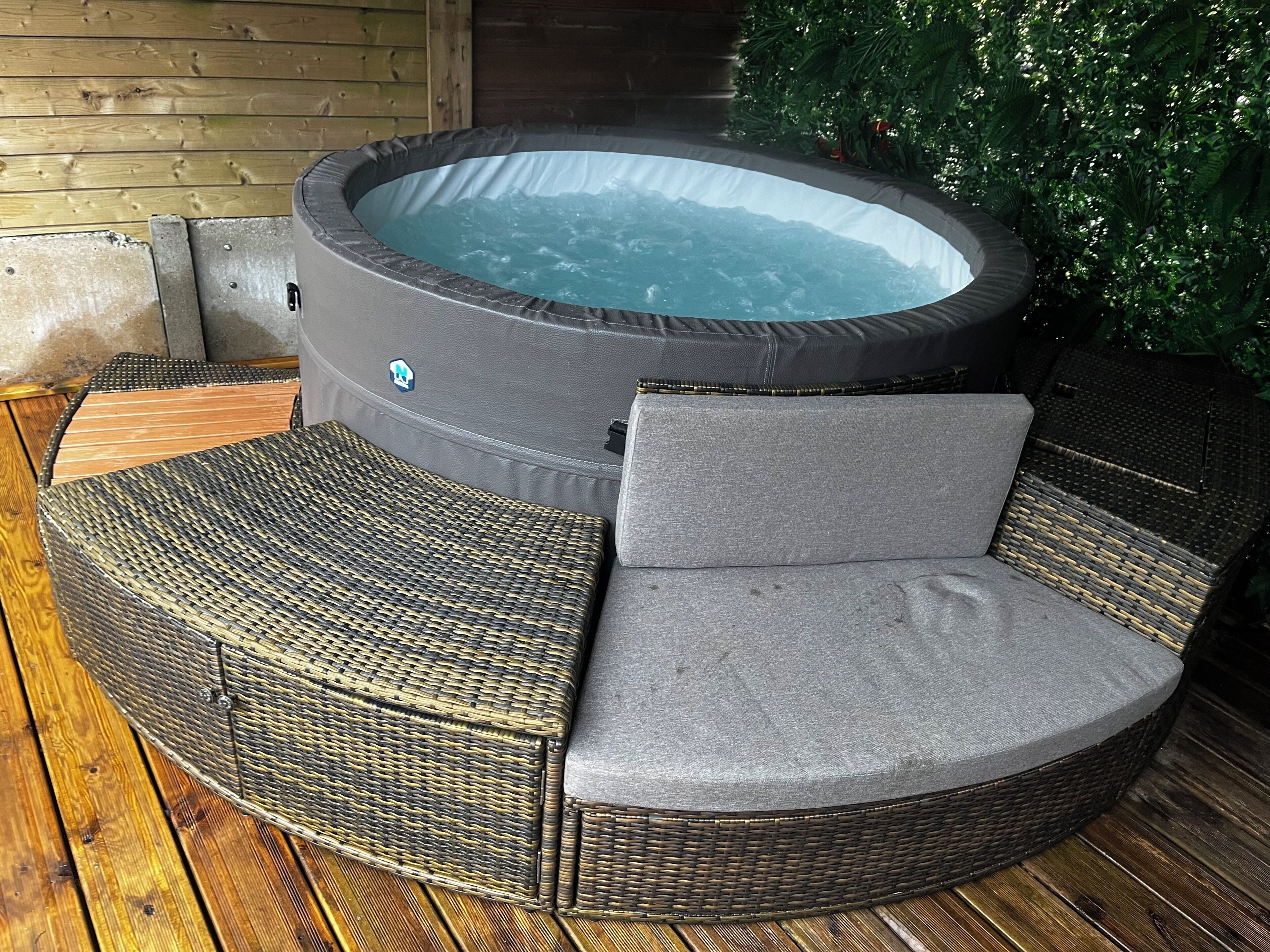 A hot tub with a wicker chair and cushion, surrounded by wooden decking.