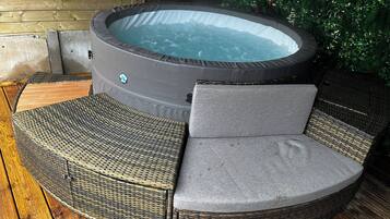 A hot tub with a wicker chair and cushion, surrounded by wooden decking.