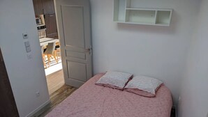 Quarto com cama, porta para banheiro e prateleira branca acima da cama.