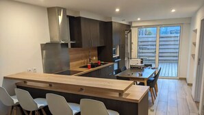 Uma cozinha moderna com armários escuros, uma ilha de madeira com banquetas e uma sala de jantar com mesa e cadeiras.