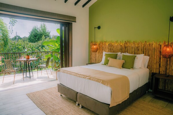 A bedroom with a large bed, a balcony with a table and chairs, and a view of greenery outside. - Tukki Ecolodge (Filandia)