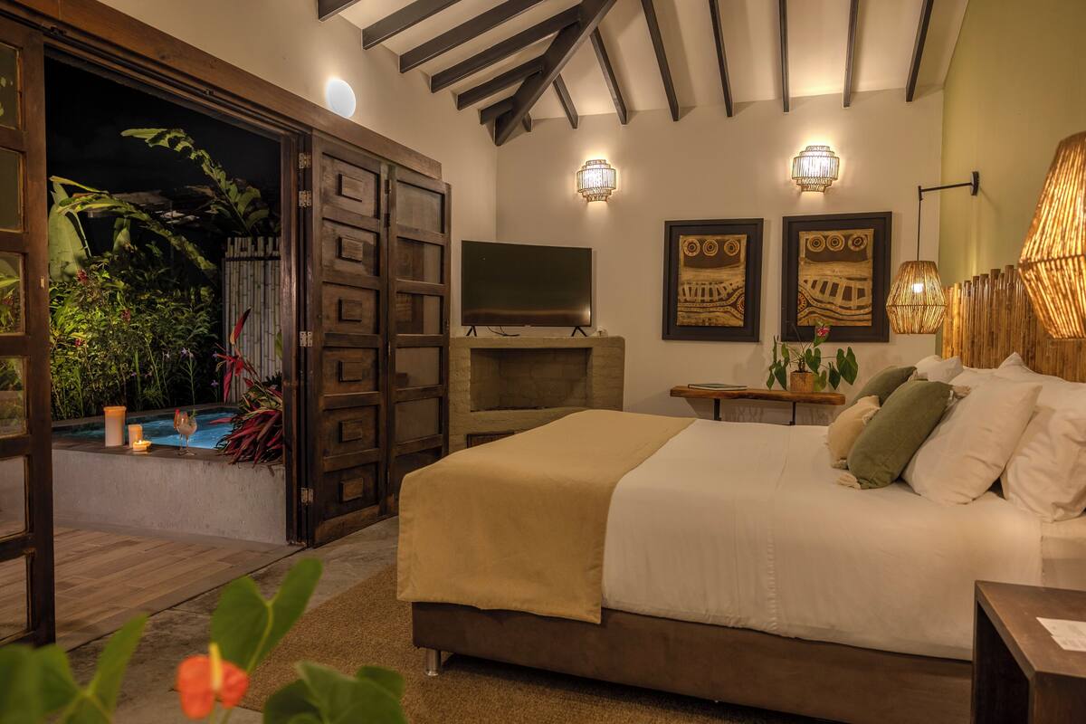 A bedroom with a bed, a TV, a wall-mounted light, and a view of a pool.