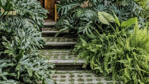 Un edificio moderno con fachada de madera, una estatua de Buda y abundante vegetación.