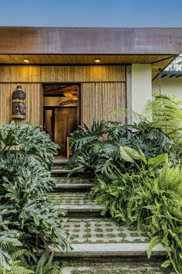 Un edificio moderno con fachada de madera, una estatua de Buda y abundante vegetación.