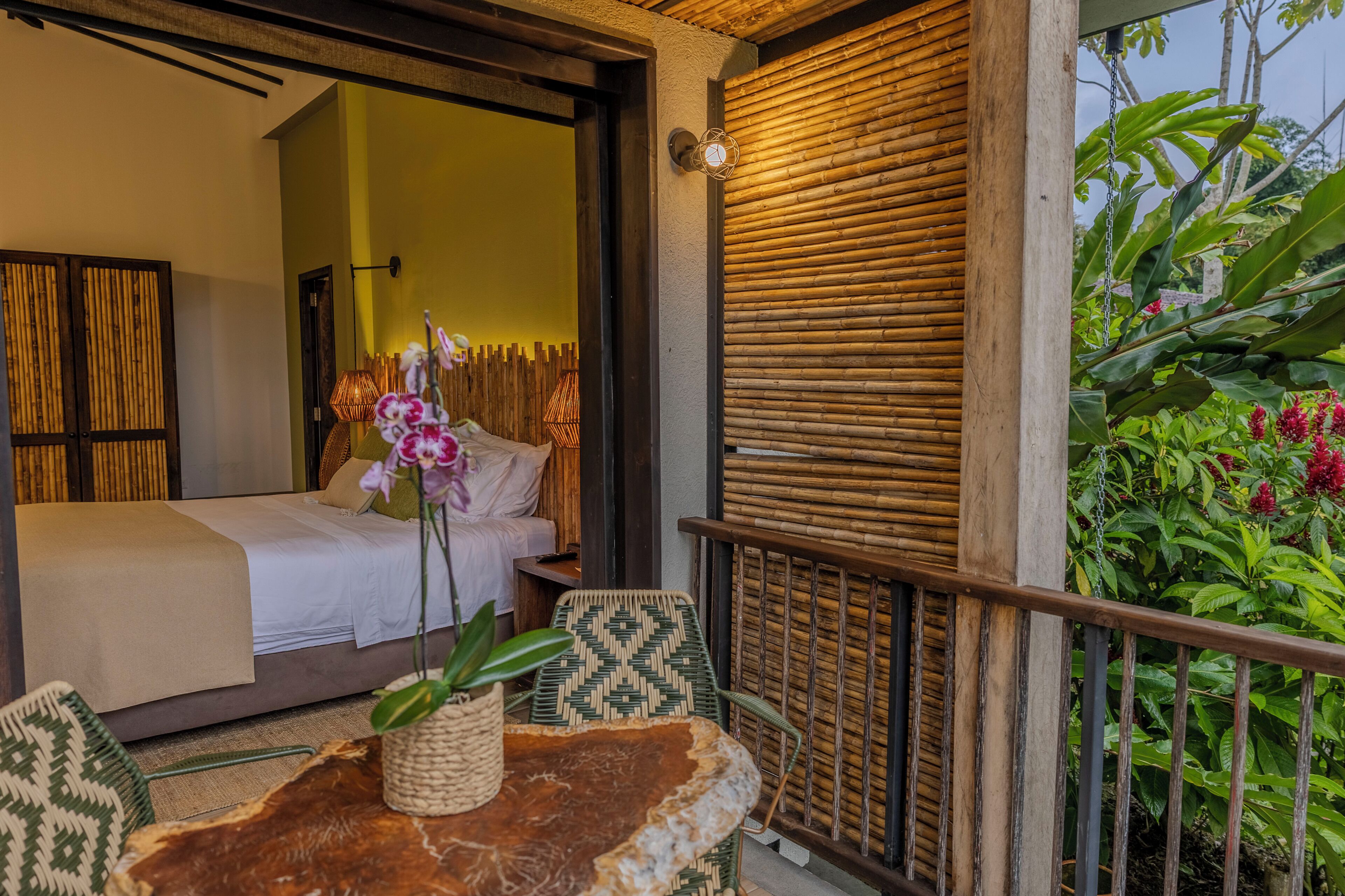 A room with a bed, a table with a plant, and a view of greenery outside.