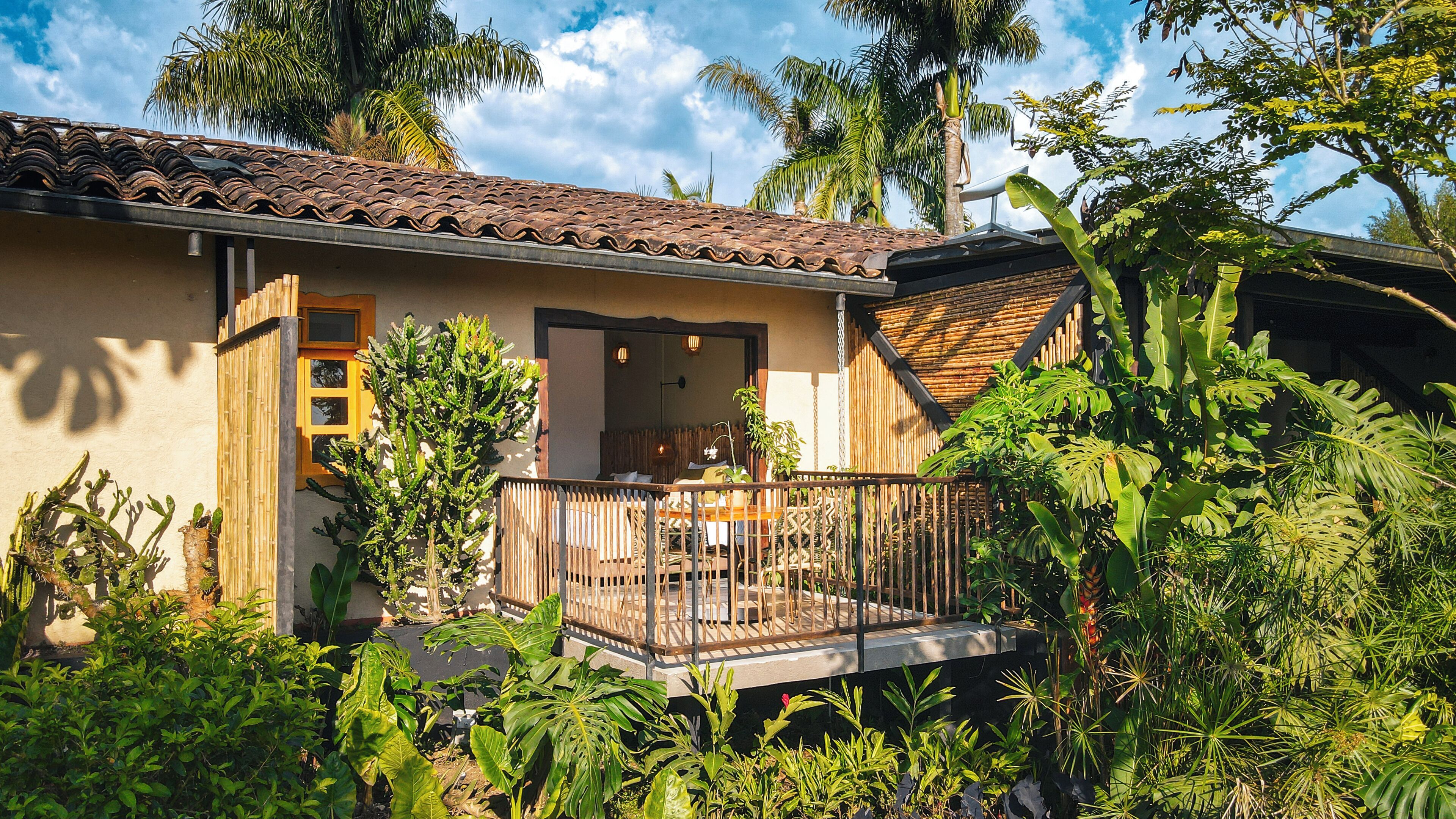 A house with a tiled roof, a wooden deck, and lush tropical vegetation.