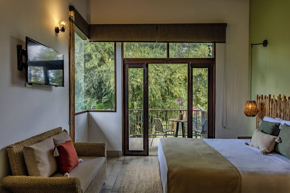A bedroom with a bed, a sofa, a TV, and a balcony with a table and chairs.