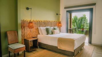 A bedroom with a bed, a chair, a nightstand, a wall-mounted lamp, and a view of greenery through an open door.