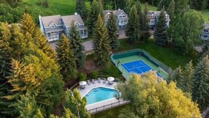 Una zona residenziale con diverse case, una piscina e un campo da tennis, il tutto circondato da una fitta foresta.