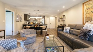 A modern living room with a leather sofa, patterned armchairs, a glass coffee table, and a dining area in the background. - A gem in the heart of Avon. Walk to the Lifts! (Avon)