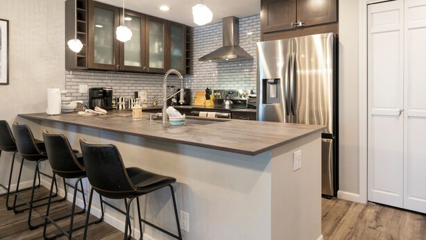 A modern kitchen with a large island, bar stools, stainless steel appliances, and dark wooden cabinets. - A gem in the heart of Avon. Walk to the Lifts! (Avon)
