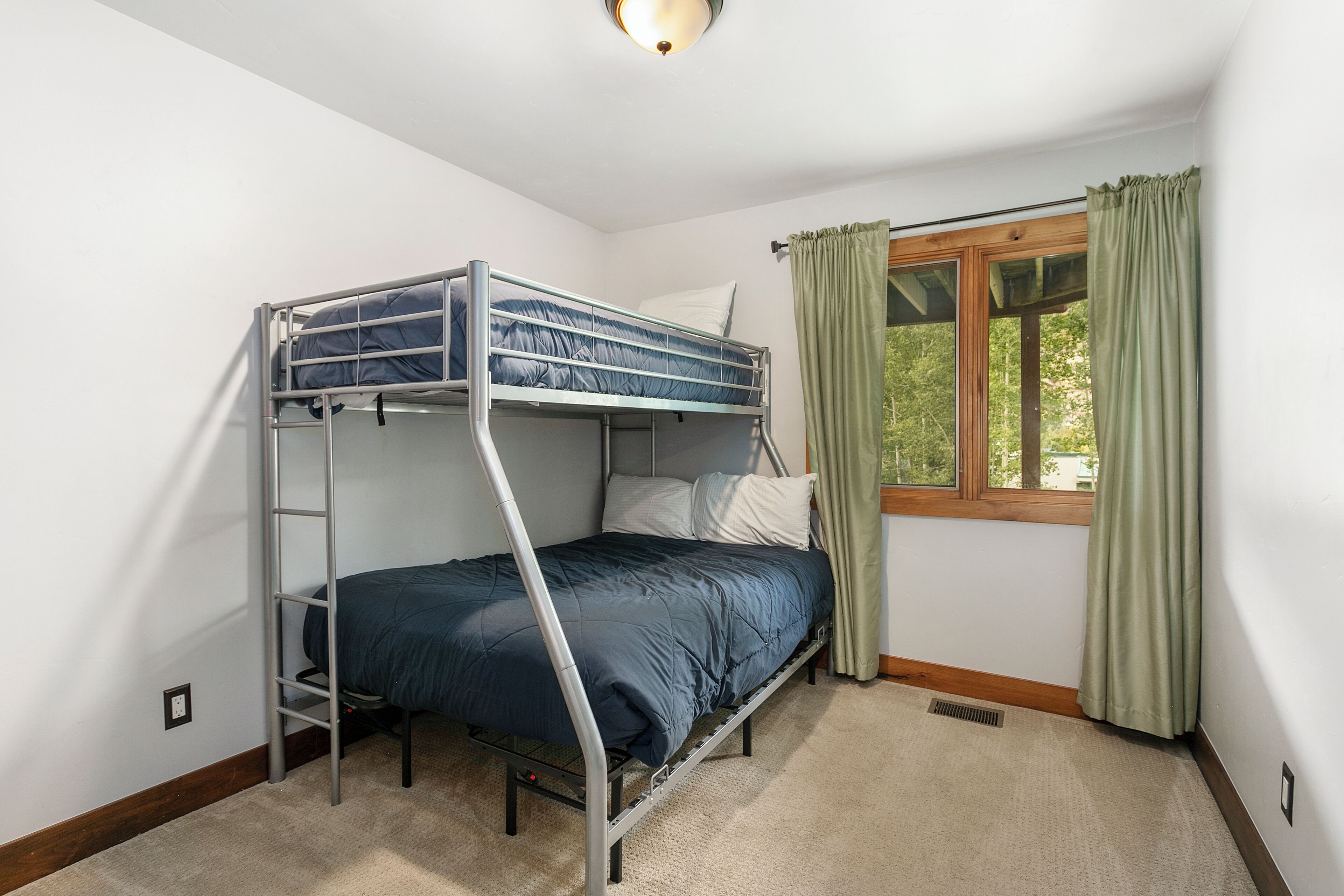 A bunk bed in a room with a window and a view of greenery outside.