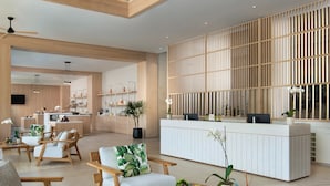 Amplia sala de estar con mobiliario de madera, un mostrador de recepción y una cocina al fondo.