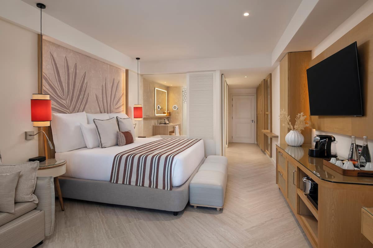 A modern hotel room with a large bed, bedside tables, a TV, and a kitchenette.