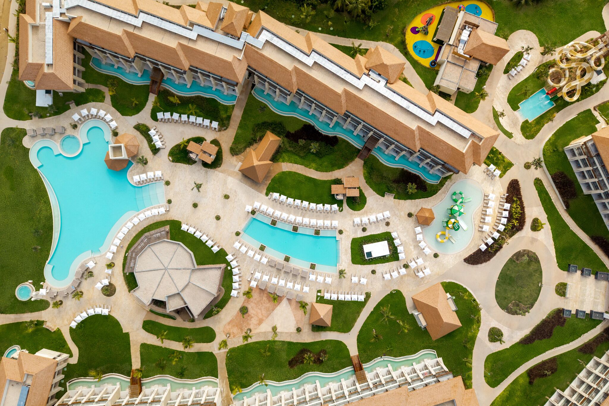 Ein Resort mit mehreren Swimmingpools, Liegestühlen und einer Wasserrutsche.