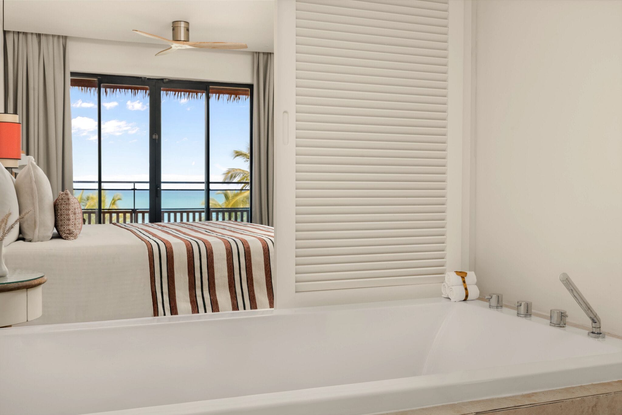 A modern bathroom with a large bathtub, a ceiling fan, and a view of the ocean through the window.