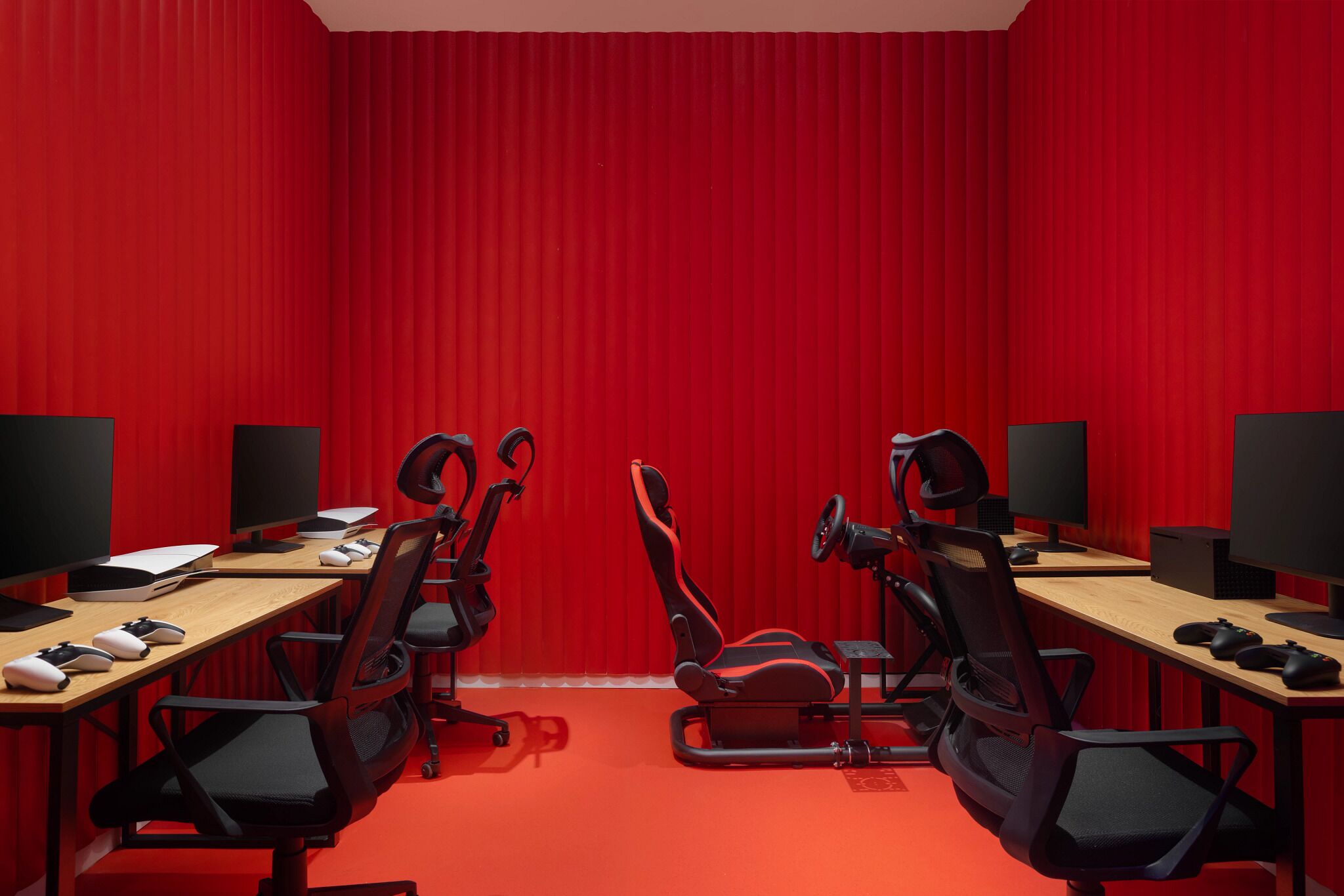 A conference room with red walls, two desks, chairs, and gaming equipment.