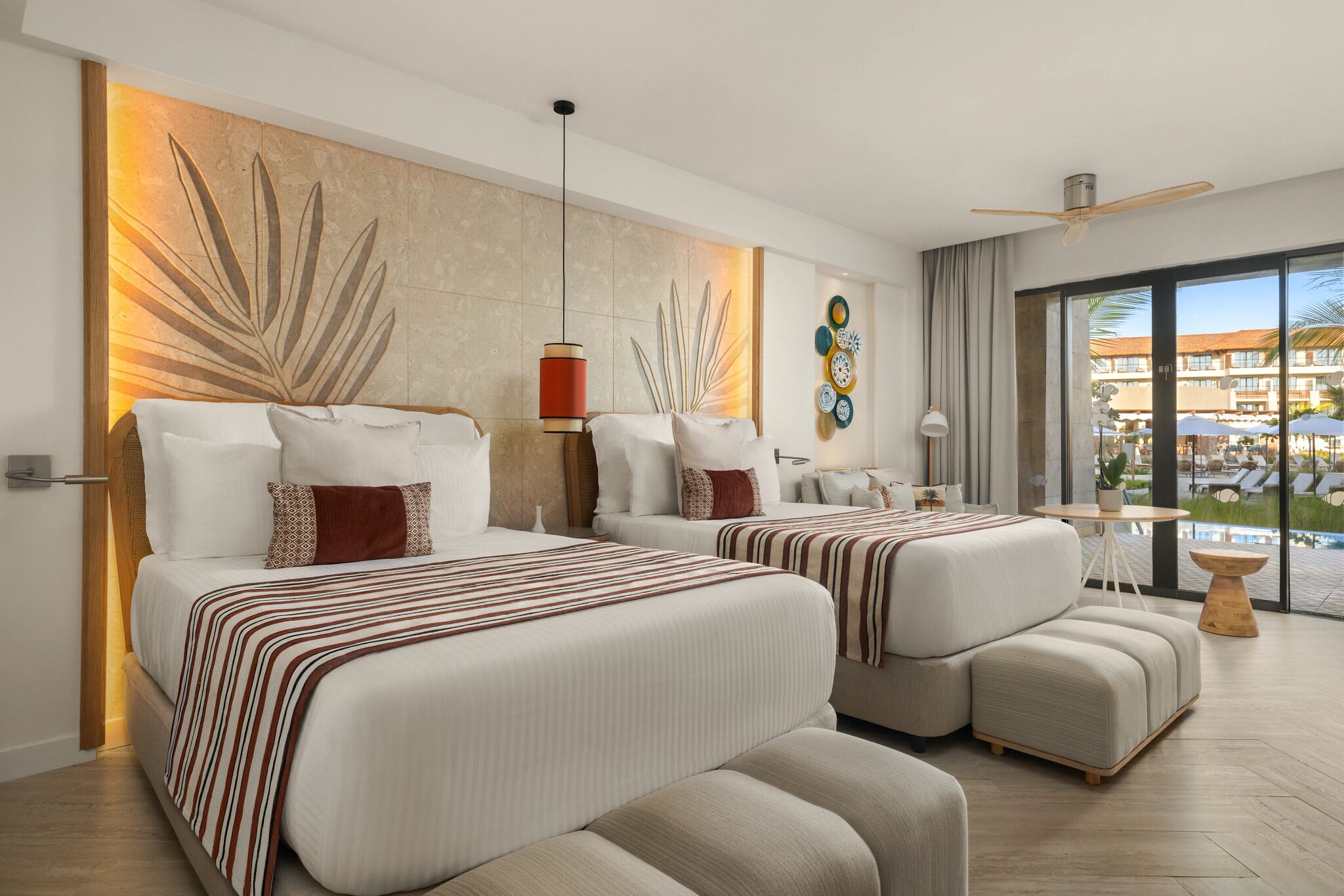 Une chambre d’hôtel avec deux lits, une grande fenêtre donnant sur la piscine et un ventilateur de plafond.