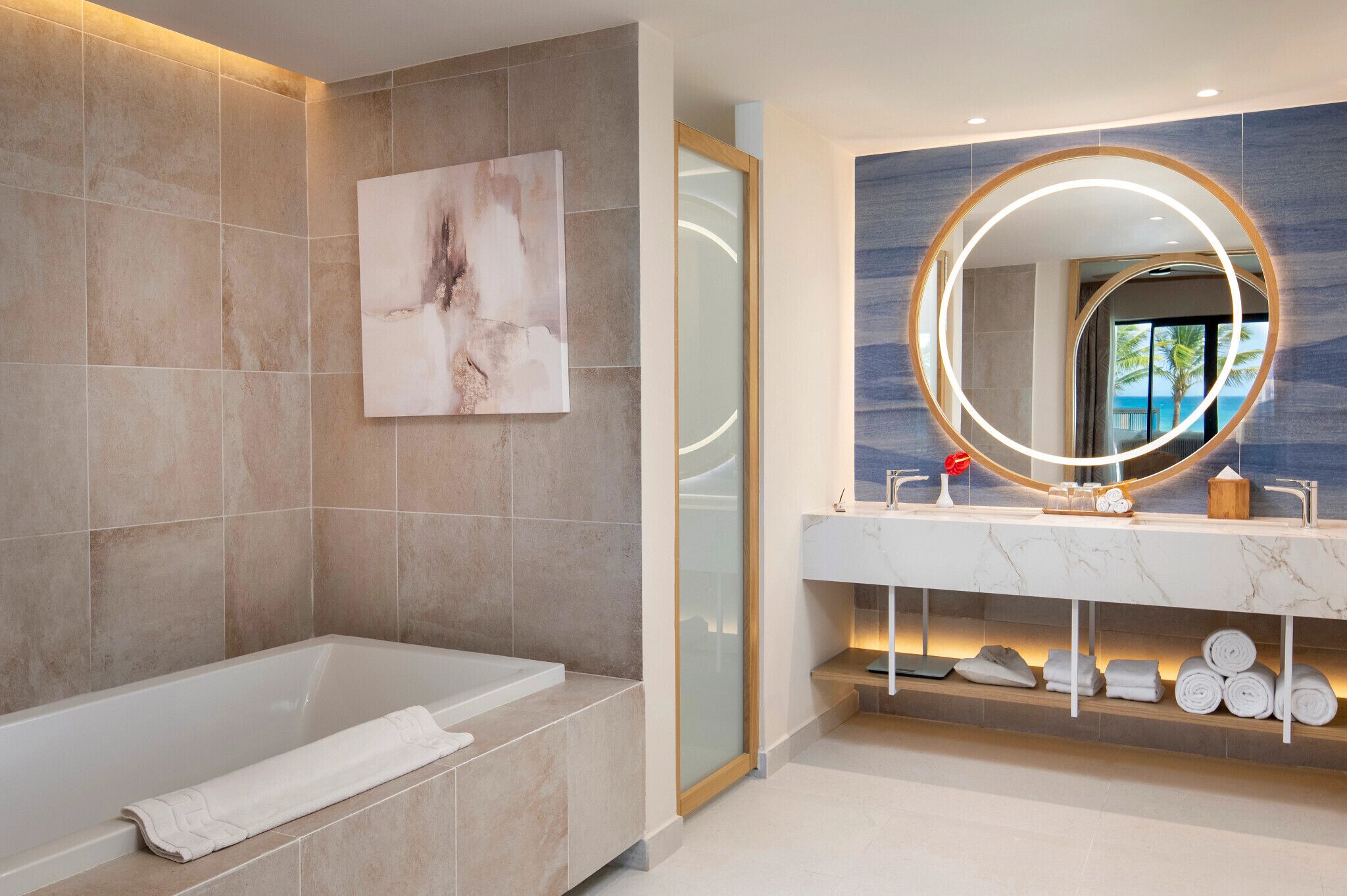 Ein modernes Badezimmer mit Badewanne, einem großen Spiegel mit runder Beleuchtung und einer Marmorarbeitsplatte.
