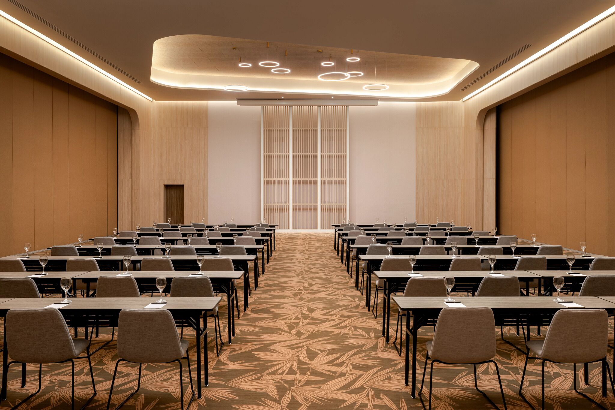 A conference room with rows of tables and chairs, a patterned carpet, and a modern ceiling design.