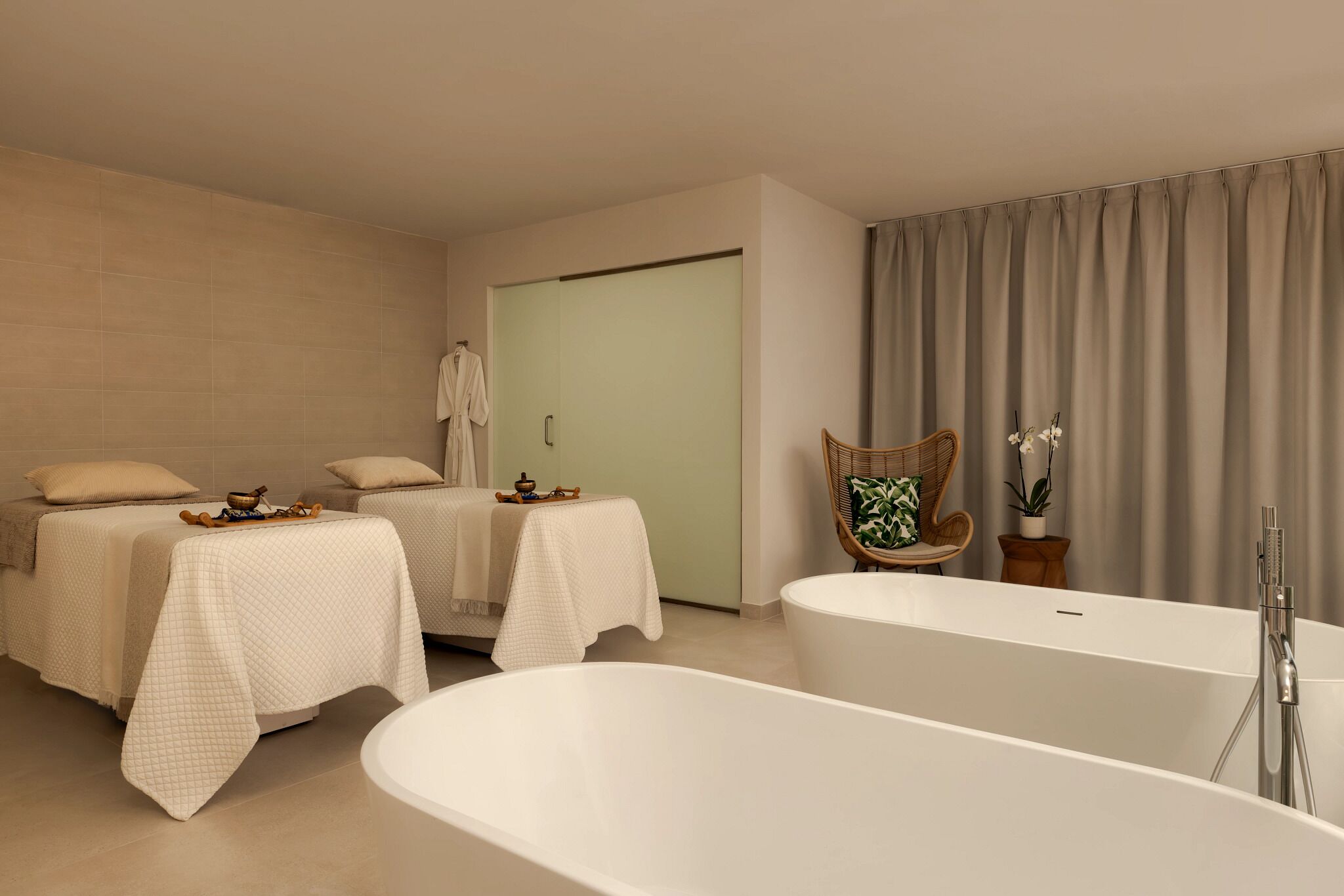 Ein moderner Spa-Raum mit zwei Massagetischen, einer großen Badewanne und einem Korbstuhl.