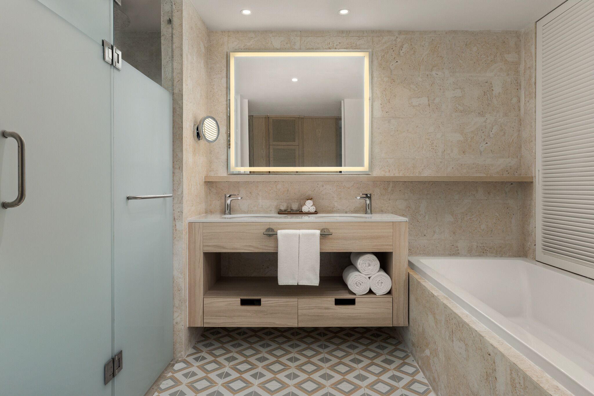 A modern bathroom with a large mirror, two sinks, a bathtub, and a patterned floor.