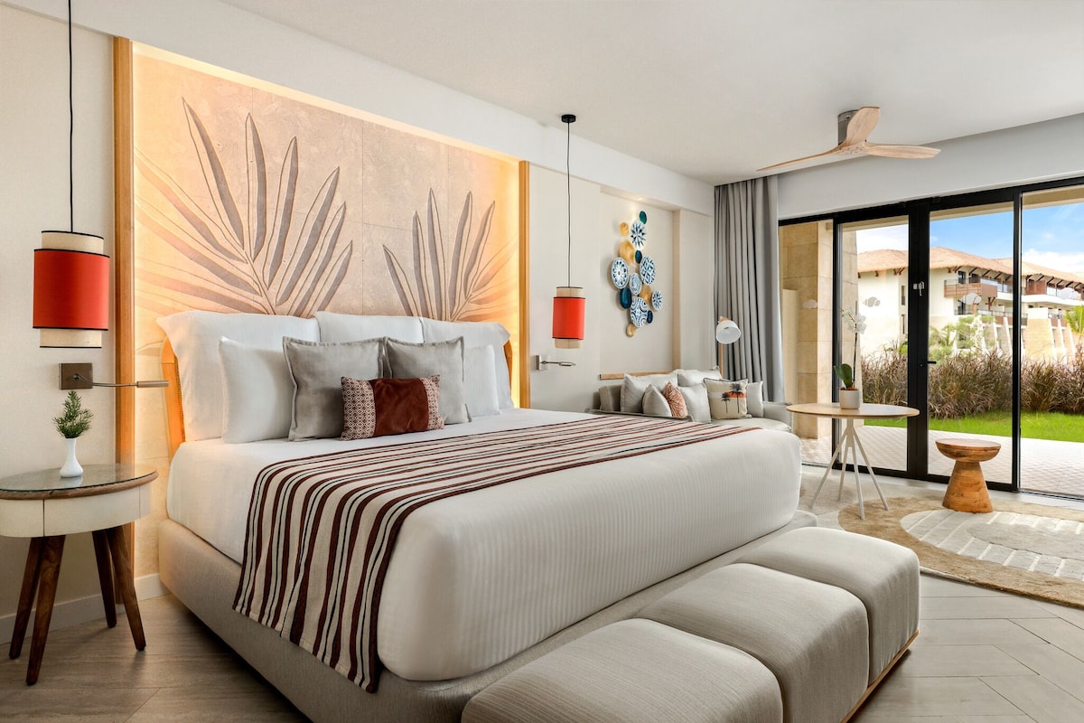 A modern bedroom with a large bed, a side table, a small round table, and a view of the outdoors.
