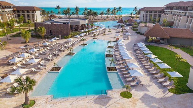 Un resort con una piscina grande, varias zonas de descanso y vistas al océano.