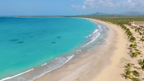 Una playa con aguas turquesas cristalinas, una orilla arenosa y un edificio de resort con techo rojo.