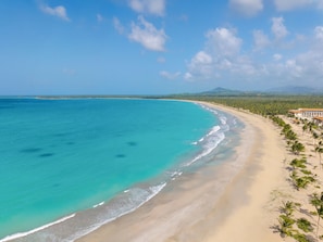 A beach with clear turquoise waters, a sandy shore, and a resort building with a red roof. - Dreams Playa Esmeralda Resort & Spa - All Inclusive (Miches)