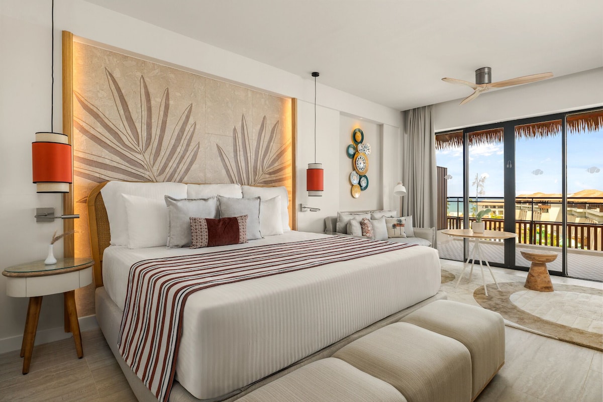 A modern hotel room with a large bed, a balcony with a view, and a ceiling fan.