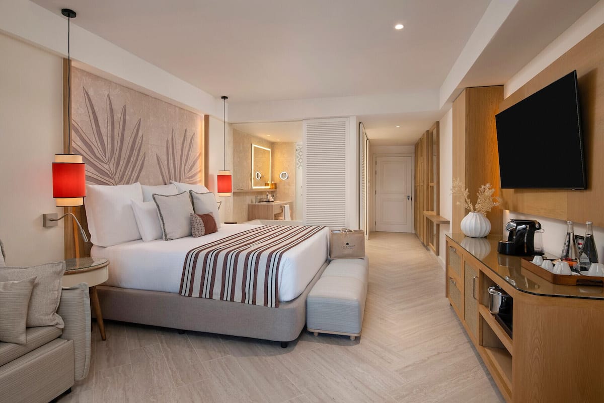 A modern hotel room with a large bed, bedside tables, a TV, and a kitchenette.