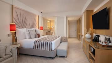 A modern hotel room with a large bed, a bedside table, a TV, a coffee maker, and a minibar.