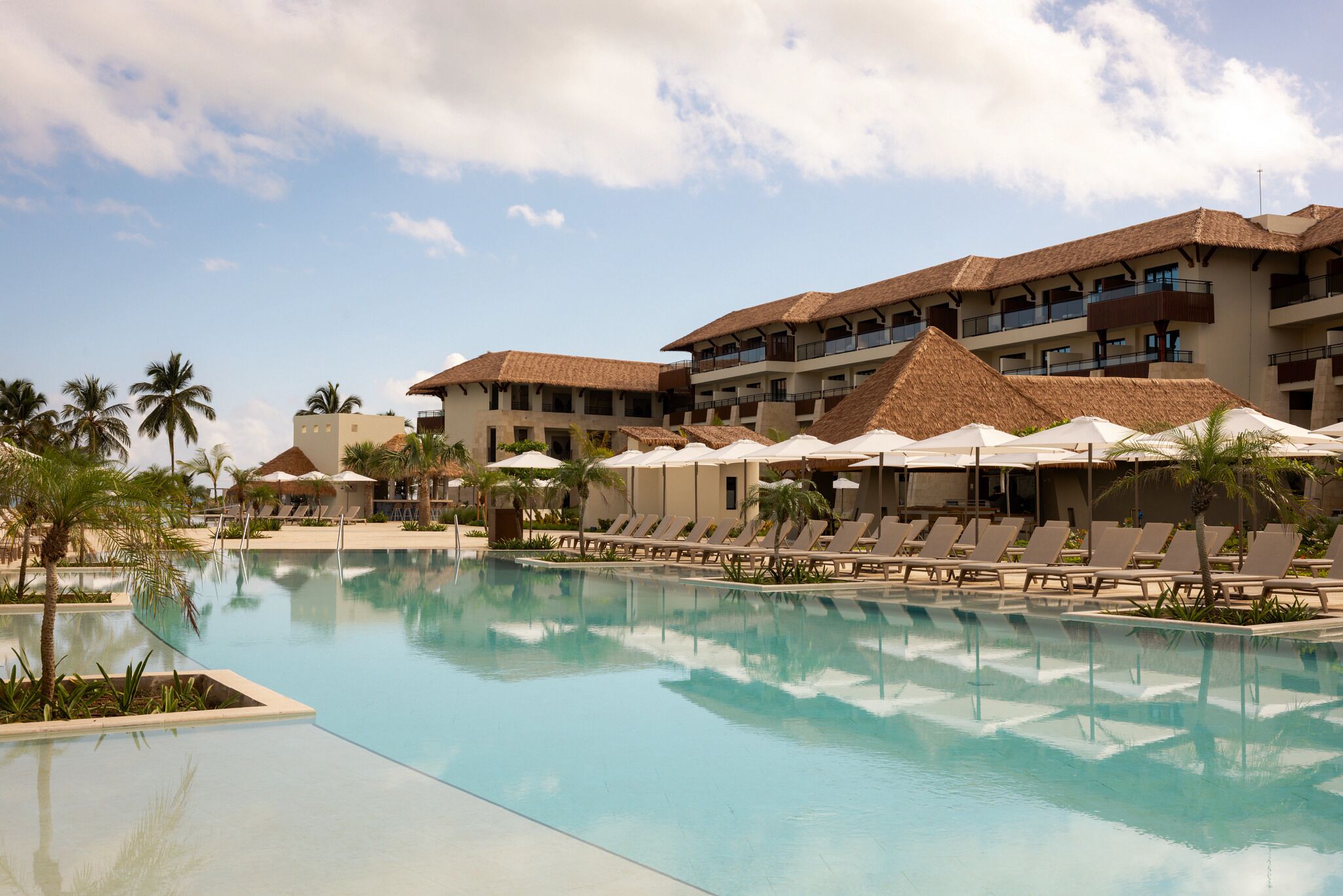 A resort pool area with lounge chairs and umbrellas, surrounded by buildings with balconies.