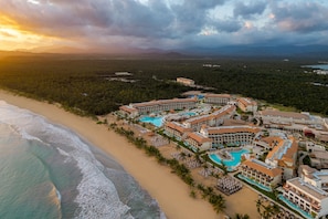 Un resort con varias piscinas, acceso directo a la playa y montañas al fondo.