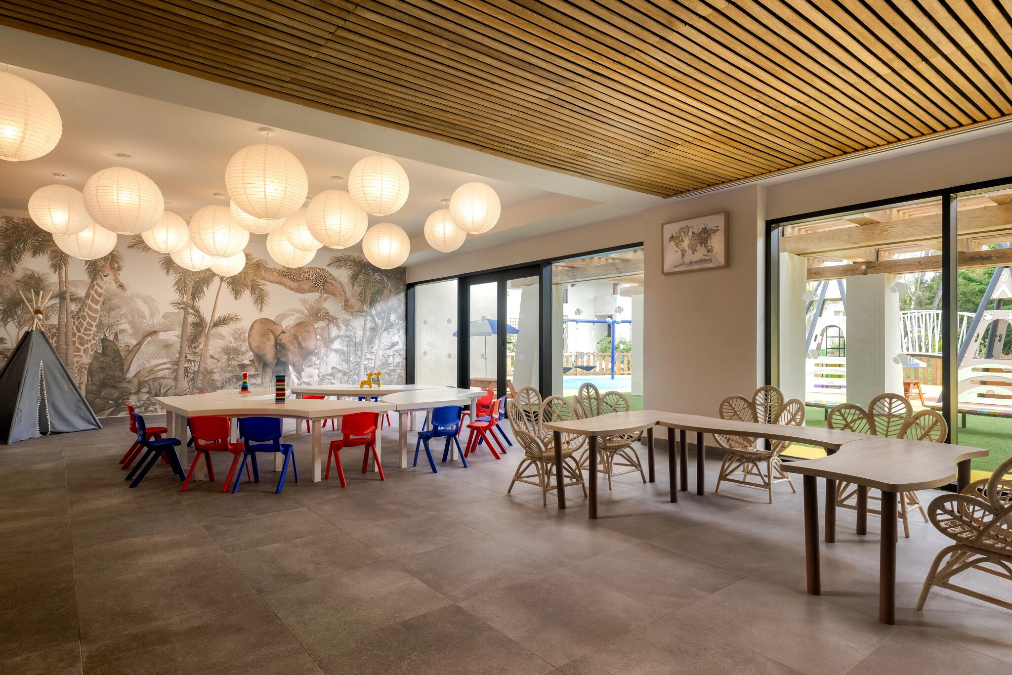 Un comedor con una gran mesa, sillas coloridas y un mural de animales.