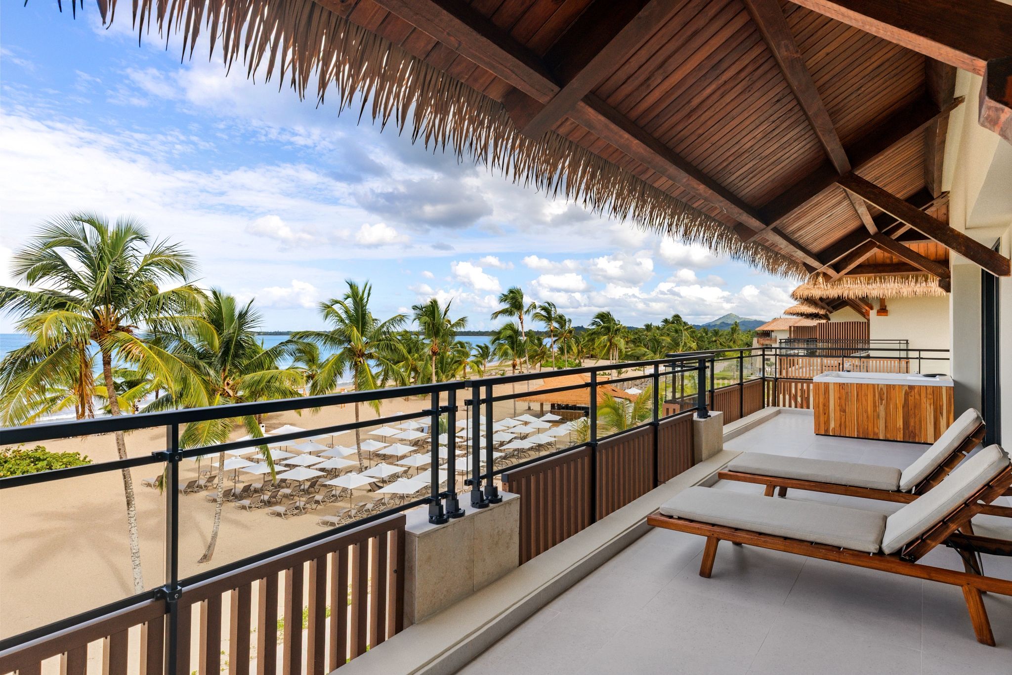 A balcony with a view of a beach, palm trees, and a mountain in the distance.