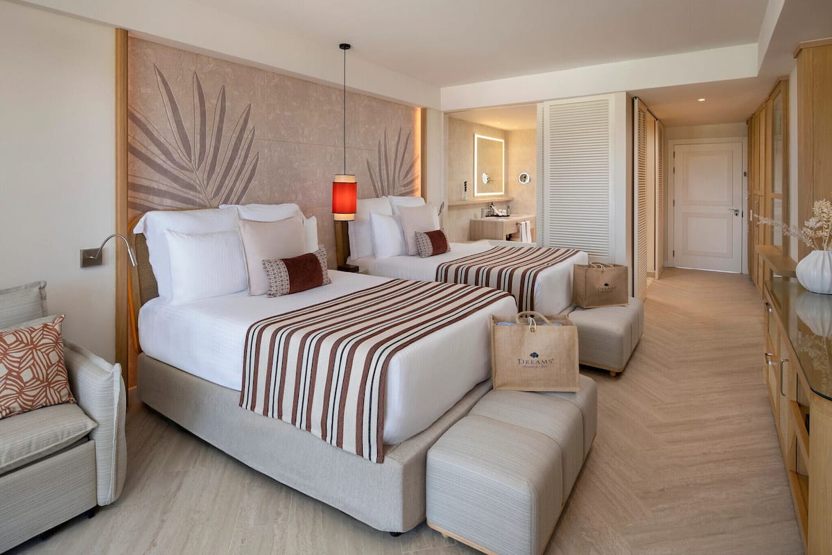 A hotel room with two beds, a sitting area, a large mirror, and a wardrobe.