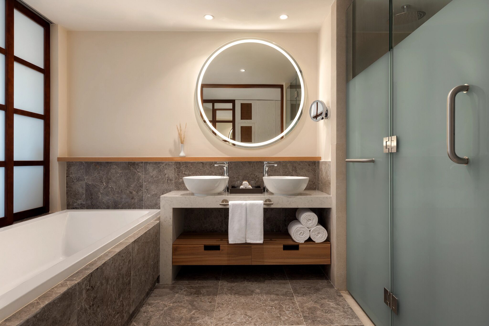 Une salle de bain moderne avec une baignoire, deux lavabos, un grand miroir et une cabine de douche en verre.