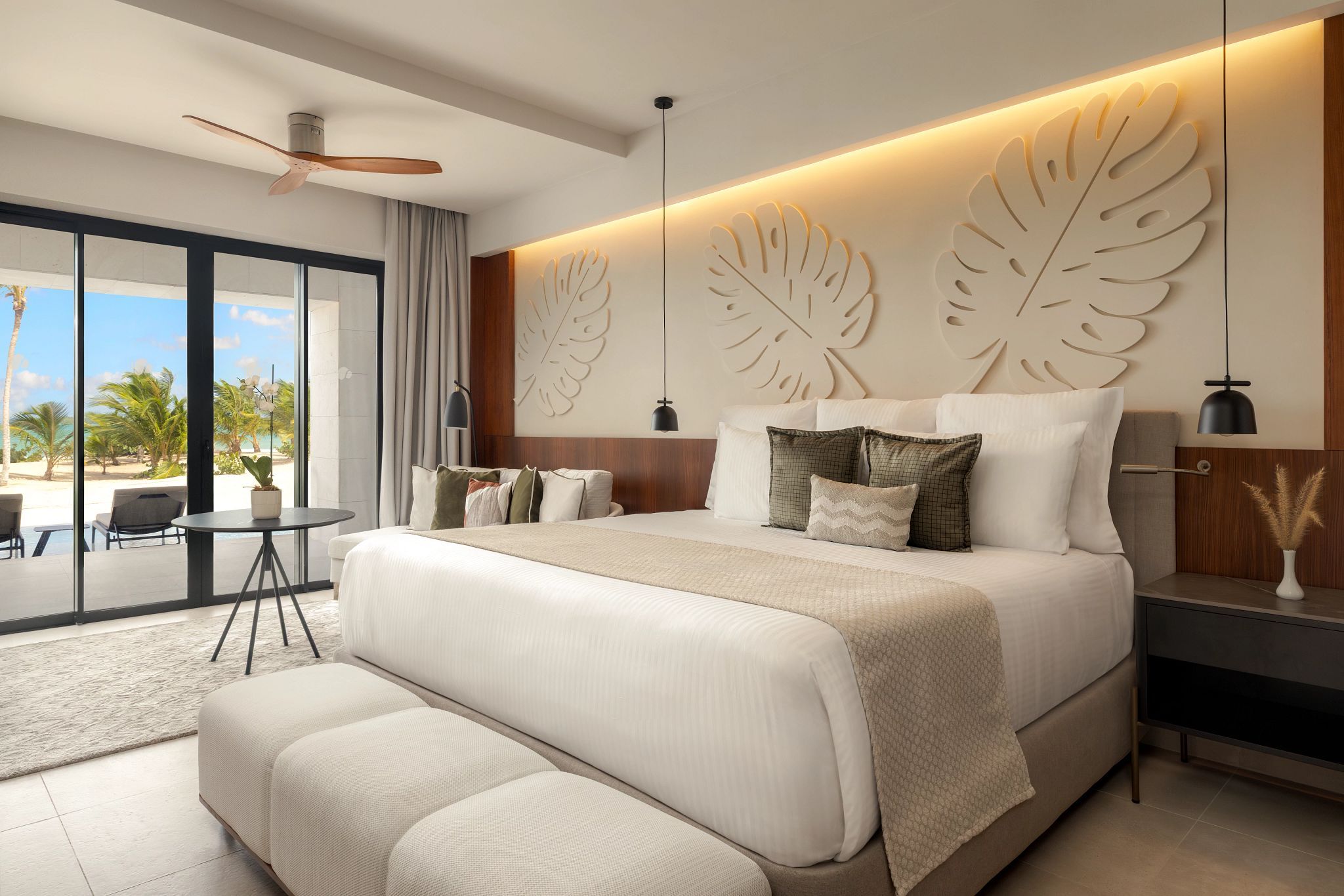 A modern bedroom with a large bed, a view of the beach, and a ceiling fan.